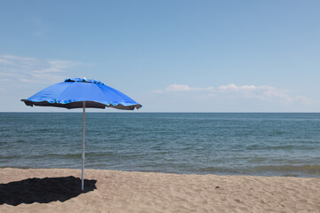 A blue beach umbrella on a sandy beach near the ocean with a blue sky
