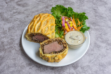 homemade Beef Wellington, tenderloin dish on wooden plate served with salad and mushroom sauce