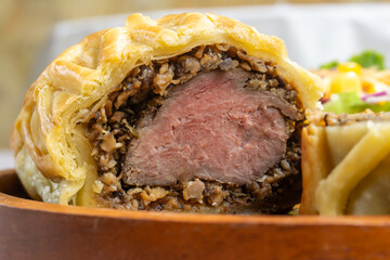 Close up of homemade Beef Wellington, tenderloin dish on wooden plate served with salad and...