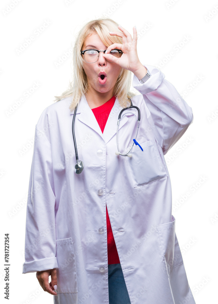 Wall mural Young beautiful blonde doctor woman wearing medical uniform over isolated background doing ok gesture shocked with surprised face, eye looking through fingers. Unbelieving expression.