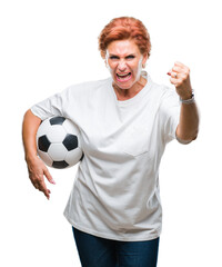 Atrractive senior caucasian redhead woman holding soccer ball over isolated background annoyed and...