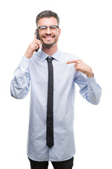 Young business adult man talking on the phone with surprise face pointing finger to himself