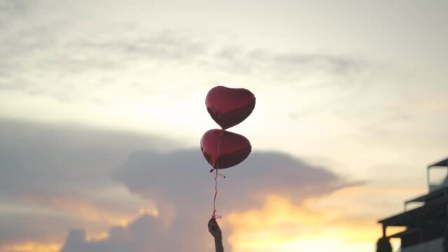 Two heart-shaped balloons float in the air held by a woman. sunset background
