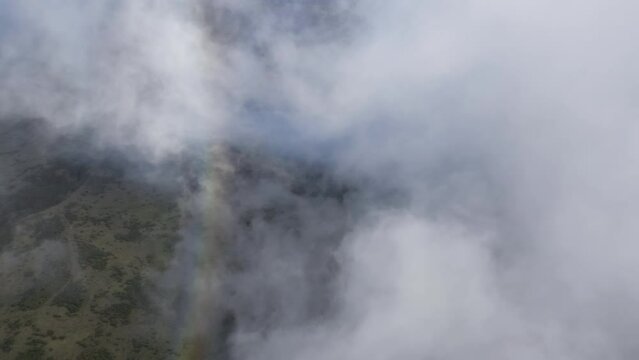 Aerial view of a colorful rainbow disappearing in white clouds over the landscape of Maui, Hawaii.