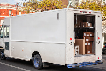 Selective blur on a white delivery van, typical from north america, in canada or in the USA, with an open door, delivering parcels, packages, and express mail, in a logistics operation.