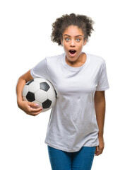 Young beautiful afro american holding soccer football ball over isolated background scared in shock...