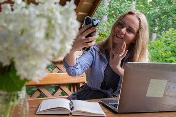 Young happy woman making video call on smartphone in wooden alcove. Relaxed outdoor setting emphasizes comfort and productivity. Remote work learning