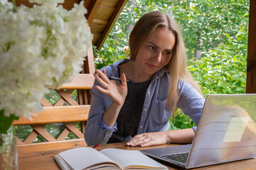 Young happy woman focuses on her laptop in wooden alcove. Relaxed outdoor setting emphasizes comfort and productivity. Remote work learning concept