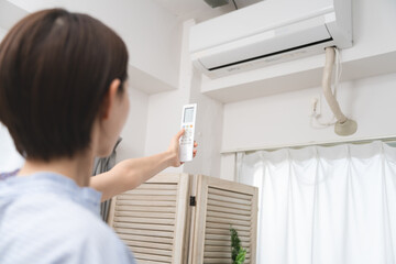 リモコンでエアコンの温度を変える若い女性　ライフスタイルイメージ