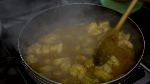 Curry Prawns Dish Stirred By A Wooden Ladle With Cooking With Steam Vapour Rising. Slow Motion Shot