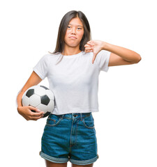 Young asian woman holding football soccer ball over isolated background with angry face, negative sign showing dislike with thumbs down, rejection concept