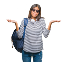 Young asian student woman wearing headphones and backpack over isolated background clueless and confused expression with arms and hands raised. Doubt concept.