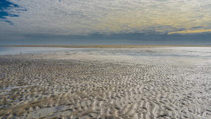 The low tide in the ocean. The wavy pattern of the sandy ridges of the exposed seabed. Puddles of...