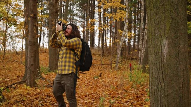 Photographer man with long hair takes photos of trees during hike in Autumn.