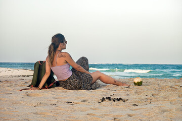 the girl is sitting on the seashore, looking into the distance, dreaming and thinking. Relax woman sitting alone thinking at the beach during sunset.