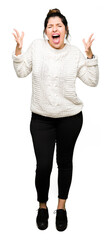 Young beautiful woman wearing winter sweater celebrating mad and crazy for success with arms raised...