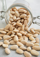 Raw white peeled almond nuts snack in glass jar on white kitchen table.Macro.