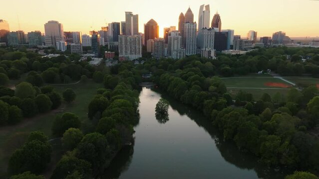Aerial drone footage of downtown Atlanta Georgia skyline at sunset with park, trees, and lake pond