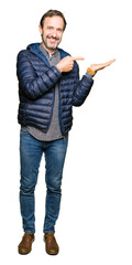Naklejka premium Middle age handsome man wearing winter coat amazed and smiling to the camera while presenting with hand and pointing with finger.