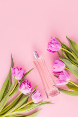 Elegant bottle of pink perfume among tulips on pink background. Top view. Flat lay. Presentation of a fragrance. Blank bottle mockup. Vertical view.
