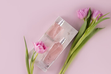Two different bottles of rose water, cosmetics, perfume lie on a marble white podium among spring flowers. Top view. Perfume concept.
