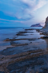 Fototapeta na wymiar Sunset at Cala Baladrar beach with the Peñon de Ifach in the background and rocks in the foreground. Sea of silk. Long exposure