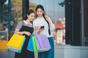 Two women are looking at their cell phones while holding shopping bags