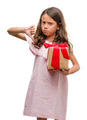 Brunette hispanic girl holding a gift with angry face, negative sign showing dislike with thumbs down, rejection concept