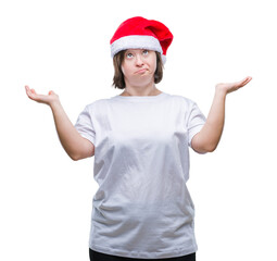 Young adult woman with down syndrome wearing christmas hat over isolated background clueless and confused expression with arms and hands raised. Doubt concept.