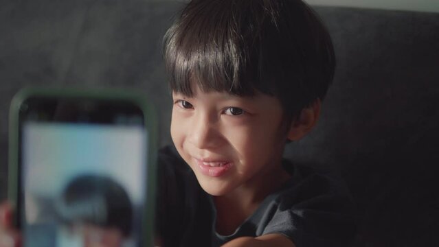 Portrait of the face of a cute Asian boy, about 5-7 years old, smiling cutely on the sofa, 4k resolution, slow motion video.

Cute Thai Asian child, 5-7 years old, holding a smartphone to take a pictu