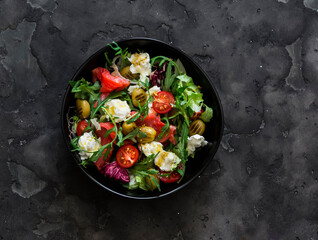 Delicious salad with vegetables, lightly salted salmon, olives, mozzarella on a dark background, top view