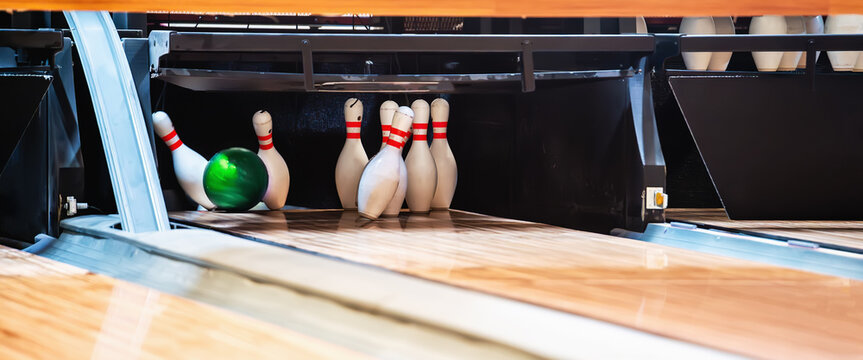 Bowling ball hits pins at end of glossy wooden bowling alley. 