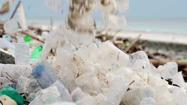 slow-motion, single-use plastic falling on littered and polluted beach
