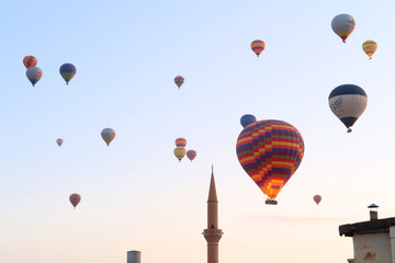 Colorful hot air balloons in the early morning over the town of Göreme with the tower of a Minaret...