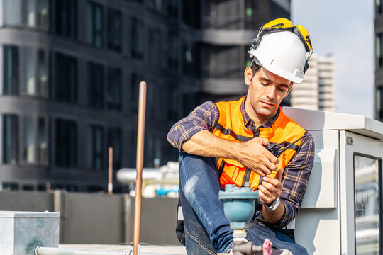 Male technical foreman inspection maintenance in safety uniform tired hot wiping sweat sitting on workshop site break relax time, Young man engineer plumbing and electrical systems on the roof