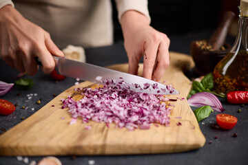 Woman chopping red Mars onion on wooden cutting board at domestic kitchen