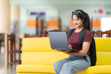 Long-haired Asian female student in high school studies using a laptop computer in a large library,...
