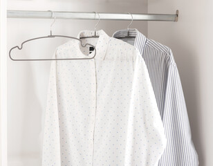 Crisp White Closet Organization with Patterned and Striped Shirts on Metal Hangers, Storage Efficiency in Modern Home Interior with Clean, Organized Appearance Emphasizing Simplicity and Order.