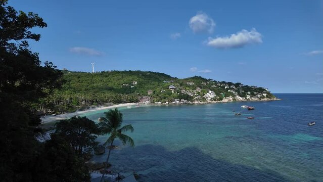 Beautiful vantage view overlooking the beach, sea, island, and boats in Koh Tao, Thailand; clear, blue water; coconut and trees and a figure of a windmill from afar; resorts and hotels are in view