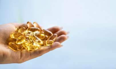 Fototapeta premium Close-up medicine yellow transparent pills, omega 3 fish oil capsules, vitamin D. Many yellow transparent capsules in hand close-up. The concept of health, vitamins, and medicine