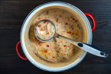 Leftovers cream fish soup in a saucepan with a ladle on a wooden table, closeup, top view - 781852150
