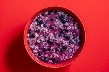 Oatmeal porridge with ripe blueberries for healthy breakfast on red background, closeup, top view - 781852186