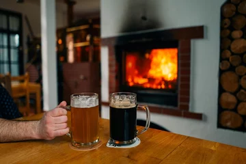 Foto op Canvas Two glasses of beer, light and dark, in a pub near the fireplace © Cavan