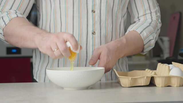 A man cracks a chicken egg into a plate, preparing to cook a dish. Perfect for culinary projects and tutorials.
