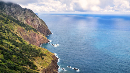 The view of the Madeira coastline, where the vast ocean meets towering cliffs under a sky adorned with wispy clouds. Nature in Madeira delights with its harmonious blend of land, water, and sky.