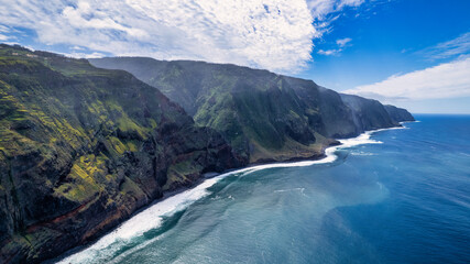 The coast of Madeira; green, rocky cliffs border with the white, frothy waves of the ocean,...