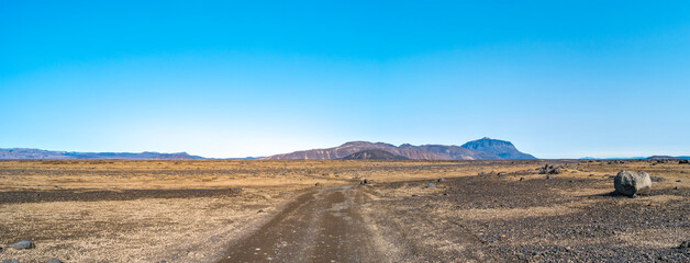 Dirt road near Herdubreid volcano in the lifeless volcanic desert in Highlands, with stones and rocks thrown by volcanic eruptions, Iceland, summer, blue sky.