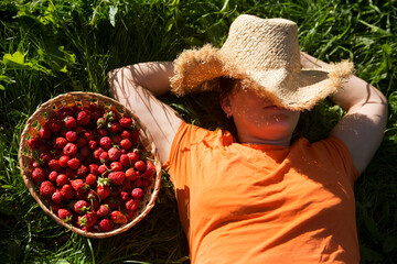 Happy  woman wearing a straw hat covering his face and an orange T-shirt laying on grass with a...