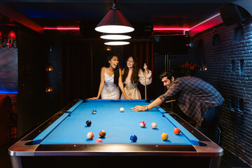 Young diversity group of people playing pool together with smile, enjoyment and fun. Young people spend time in billiards room at the nightclub. Men, women friends playing billiards. Nightlife concept - 781869152