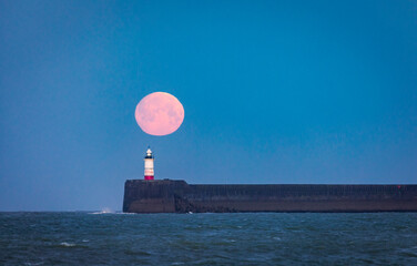 March full moon setting behind Newhaven lighthouse from Seaford beach on the east Sussex coast...